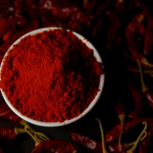 Vibrant chili powder in a bowl surrounded by dried red chilies, perfect for spice lovers.